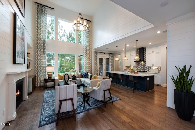 living area featuring a lit fireplace, a high ceiling, a chandelier, and dark wood finished floors