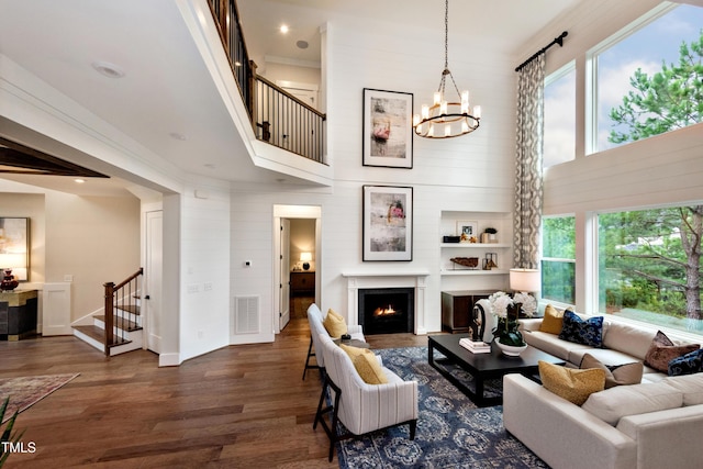 living room featuring visible vents, stairway, wood finished floors, an inviting chandelier, and a lit fireplace