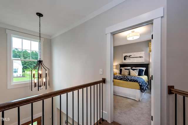 corridor featuring carpet floors, ornamental molding, an upstairs landing, and a notable chandelier