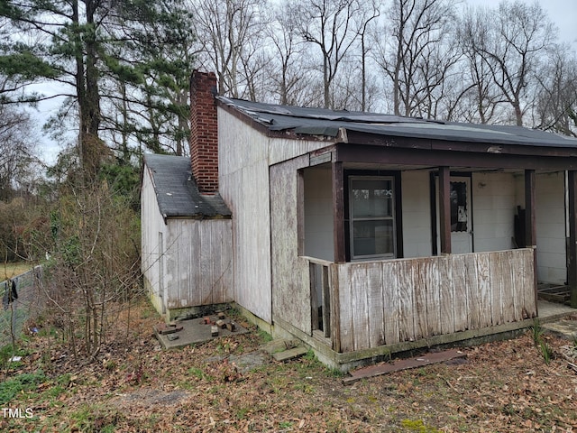 view of side of property featuring a chimney, a porch, and roof with shingles