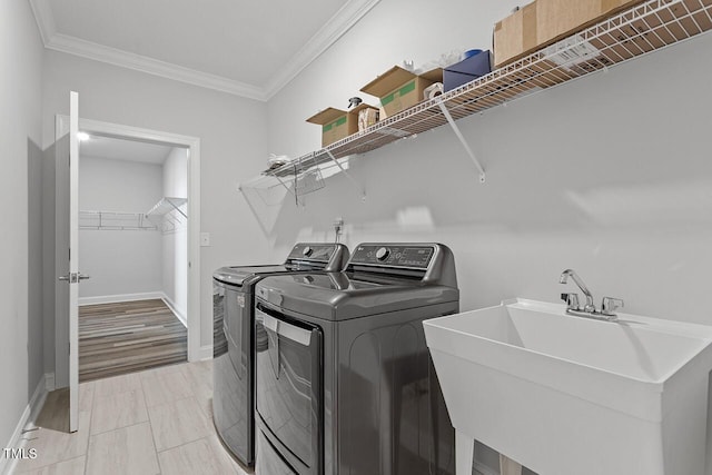 clothes washing area with laundry area, baseboards, independent washer and dryer, crown molding, and a sink