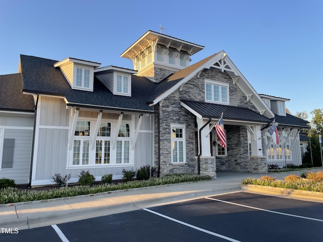 view of front of home with a shingled roof, stone siding, metal roof, uncovered parking, and board and batten siding