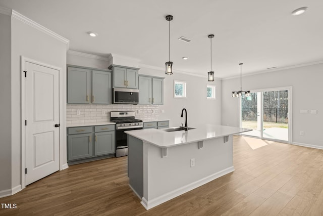 kitchen with stainless steel appliances, gray cabinets, a sink, and wood finished floors