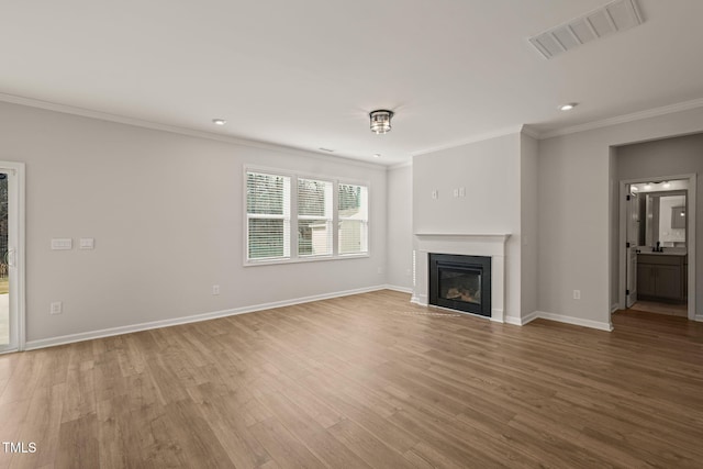 unfurnished living room featuring crown molding, visible vents, a glass covered fireplace, wood finished floors, and baseboards