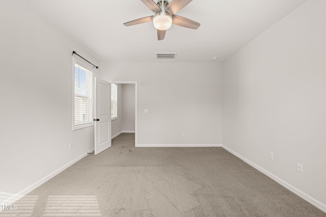 empty room with light carpet, a ceiling fan, visible vents, and baseboards