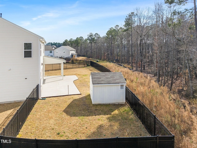 view of yard with a forest view, a fenced backyard, a storage unit, an outdoor structure, and a patio area