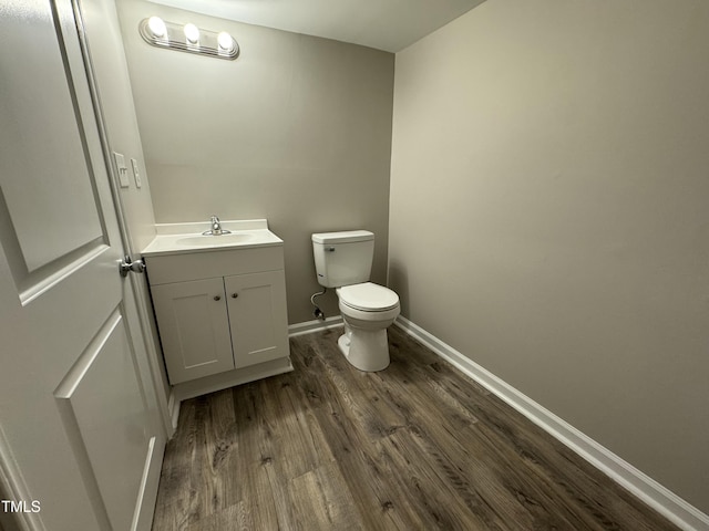 half bath with vanity, toilet, wood finished floors, and baseboards