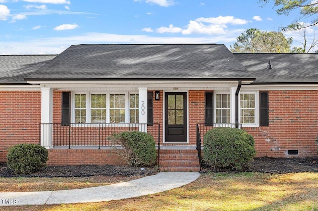 view of front of home with a porch, crawl space, roof with shingles, and brick siding