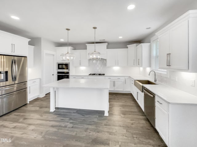 kitchen with decorative backsplash, a kitchen island, wood finished floors, stainless steel appliances, and a sink