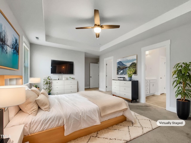 carpeted bedroom with visible vents, a raised ceiling, baseboards, ceiling fan, and ensuite bath