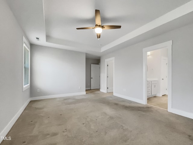 carpeted empty room featuring a raised ceiling and baseboards