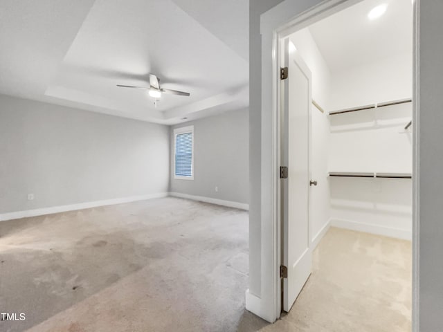 unfurnished room featuring carpet floors, a raised ceiling, ceiling fan, and baseboards