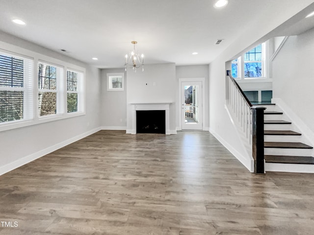 unfurnished living room with recessed lighting, plenty of natural light, wood finished floors, and stairs