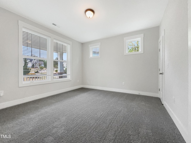 empty room featuring visible vents, baseboards, and dark carpet