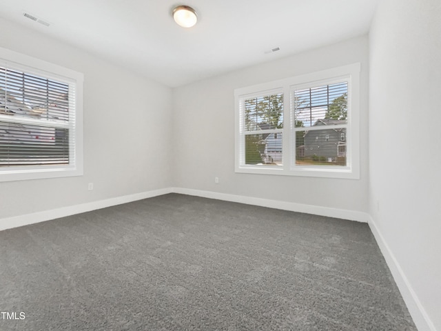 empty room featuring visible vents, baseboards, and dark colored carpet
