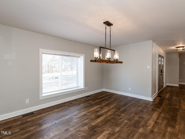 empty room with dark wood-style floors, an inviting chandelier, visible vents, and baseboards