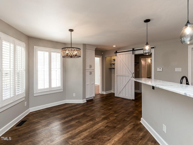 unfurnished dining area featuring visible vents, dark wood finished floors, baseboards, and a barn door