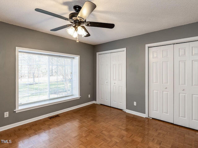 unfurnished bedroom with two closets, visible vents, a ceiling fan, a textured ceiling, and baseboards