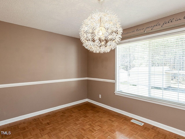 empty room featuring a chandelier, visible vents, a textured ceiling, and baseboards