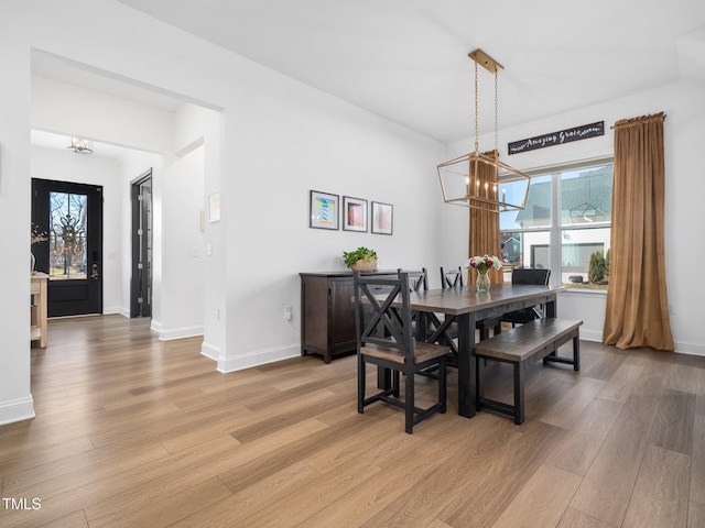 dining space with light wood-type flooring, baseboards, and an inviting chandelier