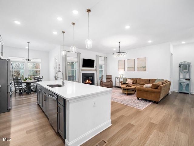 kitchen featuring light wood finished floors, a warm lit fireplace, stainless steel appliances, light countertops, and a sink