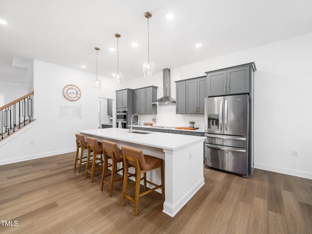 kitchen with appliances with stainless steel finishes, an island with sink, wall chimney range hood, and dark wood finished floors