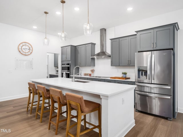 kitchen featuring a center island with sink, wall chimney exhaust hood, appliances with stainless steel finishes, dark wood-type flooring, and a sink