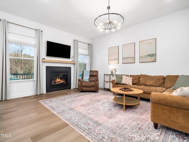 living area with light wood-type flooring, plenty of natural light, a glass covered fireplace, and a notable chandelier