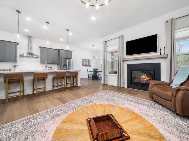 living area with a glass covered fireplace, light wood-style flooring, recessed lighting, and an inviting chandelier