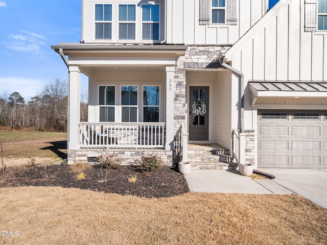 doorway to property with a porch, concrete driveway, board and batten siding, a standing seam roof, and stone siding