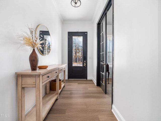 doorway to outside featuring baseboards, light wood-style flooring, and crown molding