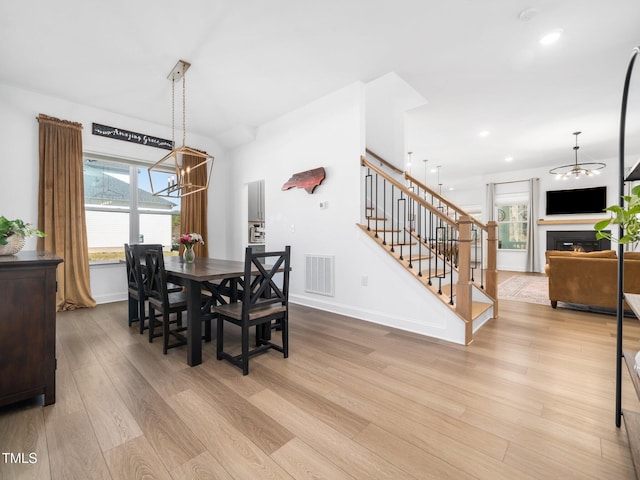 dining space with visible vents, light wood-style flooring, stairway, a lit fireplace, and baseboards