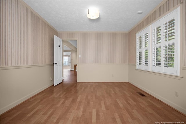 unfurnished room featuring a textured ceiling, wood finished floors, visible vents, and baseboards