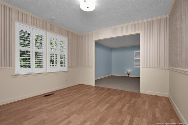 unfurnished room featuring a textured ceiling, wood finished floors, visible vents, and crown molding