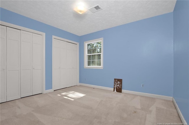 unfurnished bedroom featuring baseboards, visible vents, multiple closets, and carpet flooring