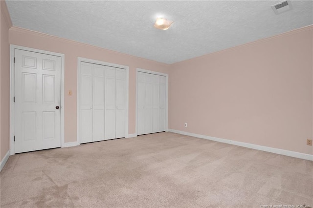 unfurnished bedroom featuring two closets, visible vents, carpet flooring, a textured ceiling, and baseboards