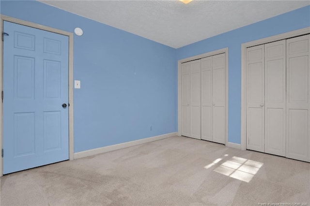 unfurnished bedroom with baseboards, a textured ceiling, carpet flooring, and multiple closets