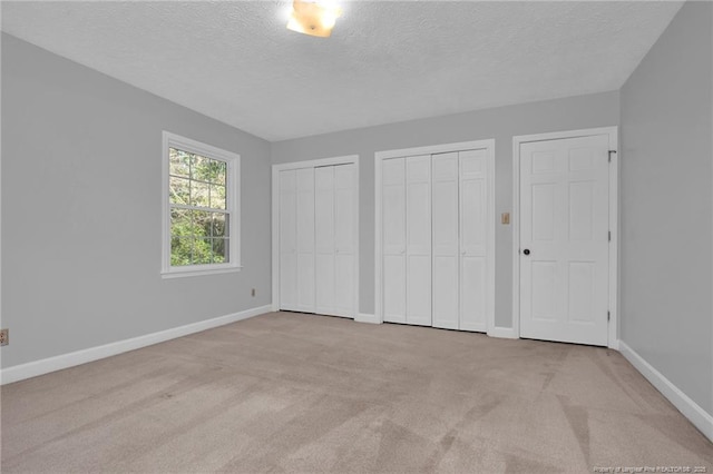 unfurnished bedroom with carpet, a textured ceiling, baseboards, and two closets