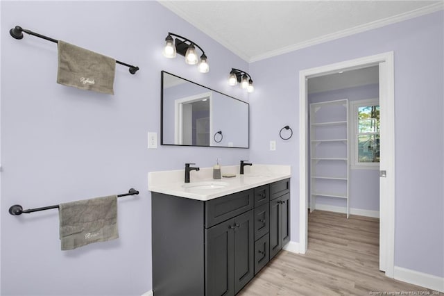 bathroom featuring baseboards, wood finished floors, a sink, and crown molding