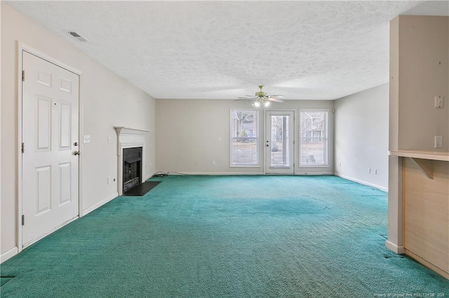 unfurnished living room with a textured ceiling, carpet floors, a fireplace with flush hearth, visible vents, and a ceiling fan