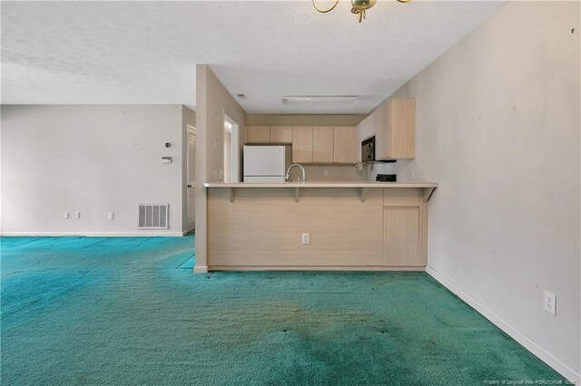 kitchen with visible vents, light brown cabinetry, freestanding refrigerator, light carpet, and black microwave