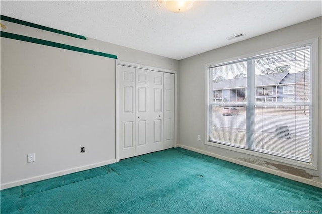 unfurnished bedroom featuring carpet floors, a closet, visible vents, a textured ceiling, and baseboards