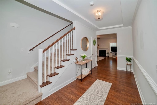 staircase with a fireplace, baseboards, a raised ceiling, and wood finished floors