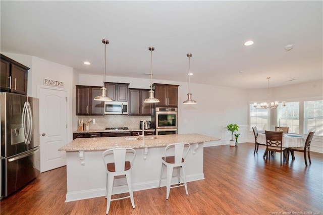 kitchen with stainless steel appliances, backsplash, a sink, dark brown cabinets, and wood finished floors