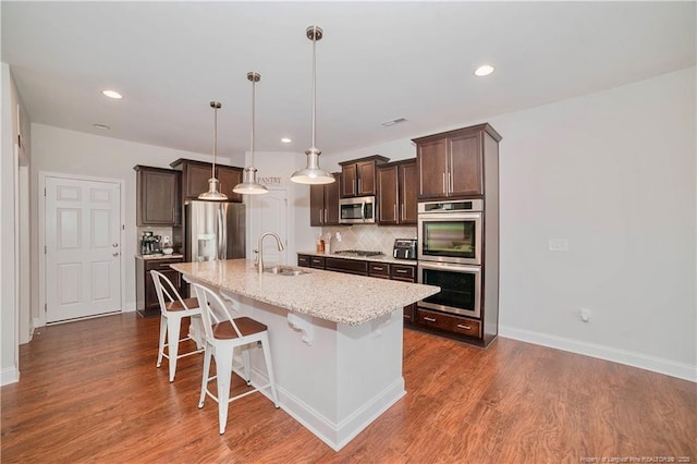 kitchen featuring decorative backsplash, appliances with stainless steel finishes, a sink, dark brown cabinetry, and a kitchen breakfast bar