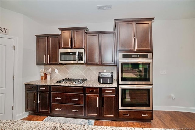 kitchen with visible vents, light stone counters, wood finished floors, stainless steel appliances, and backsplash