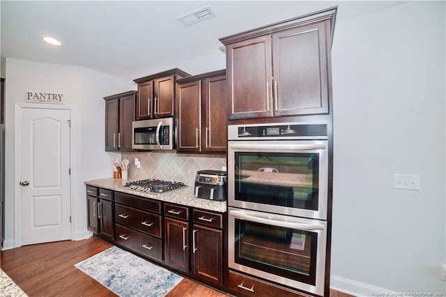 kitchen featuring dark brown cabinetry, wood finished floors, visible vents, appliances with stainless steel finishes, and tasteful backsplash