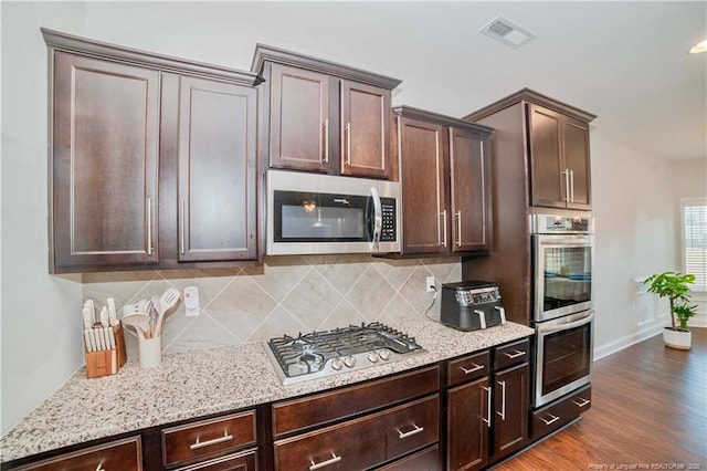 kitchen featuring dark wood finished floors, stainless steel appliances, tasteful backsplash, visible vents, and dark brown cabinets