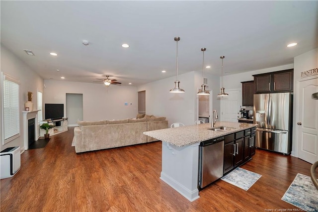 kitchen with stainless steel appliances, visible vents, dark wood-type flooring, a sink, and light stone countertops