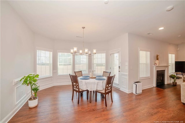 dining space featuring a fireplace with raised hearth, a chandelier, a decorative wall, and wood finished floors